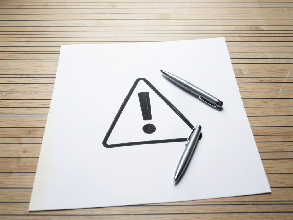A sheet of paper with a warning triangle and an exclamation mark, with a pen, symbolizing caution.